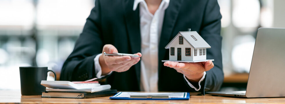 Businessman or real estate agents holding house model offering to his client after signing the sale at the office.