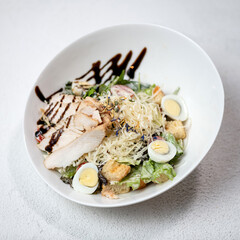Caesar salad. Salad with bread croutons. Salad with baked chicken fillet, eggs, parmesan, lettuce, tomatoes on black plate. Caesar salad. Healthy diet. Low calorie food. Top view. White background