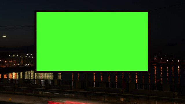 Timelapse of green screen billboard with night traffic. lightbox with chroma key on city street at night . reflection of streetlights on water. Commercial public information and advertising marketing