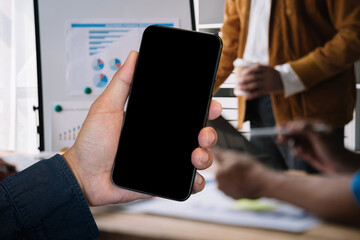 Business - technology and office concept - Hand holding mobile phone with blank screen in office.