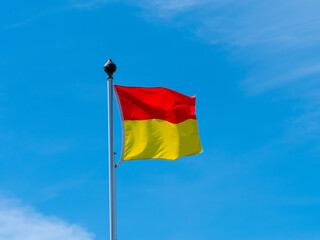 A red and yellow flag allowing swimming on the beach. flag on a blue sky background.