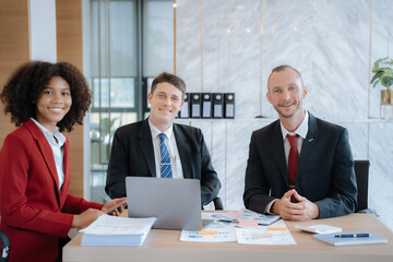 Business team smiling and confident standing in front of bright desk.