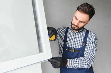 Workman in overalls installing or adjusting plastic windows in the living room at home