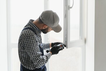 Workman in overalls installing or adjusting plastic windows in the living room at home