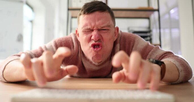 Excited grimacing internet fraud guy types on PC keyboard at table slow motion. Crazy man prepares provocation online. Emotional gamer plays in room