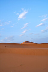 Fototapeta na wymiar A portrait shot of the sand dunes in the Sahara desert, Morocco, on a blue sky day with clouds.