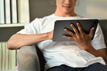 Cropped image of adult asian man working, browsing internet on digital tablet. People, technology and lifestyle