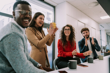 A happy black male person said something stupid. His white colleagues are applauding and laughing at him. They are having fun moments at work