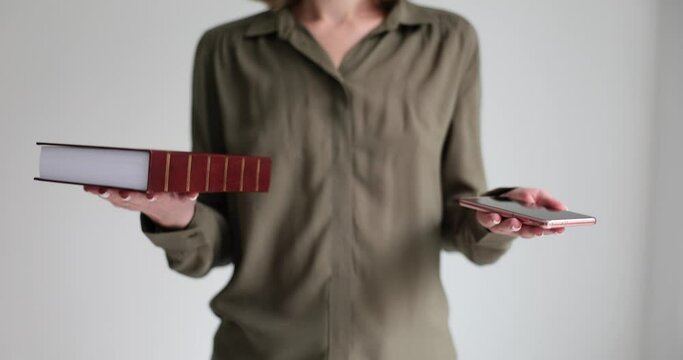 Woman intuitively measures weight of thick book and mobile phone in hands. Woman lifting objects compares traditional and modern technologies slow motion