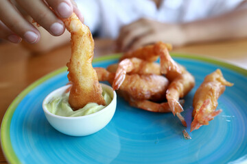 Person dipping battered shrimp in sauce