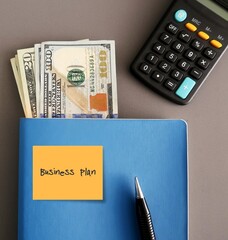 Blue notebook, money cash dollars, calculator with written text BUSINESS PLAN document that defines...