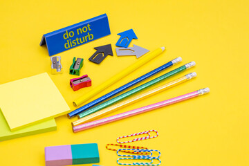 On the table in the office, pencils, stickers, paper clips, sharpeners, note paper as a concept of office work offline on a yellow background