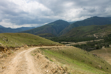 Fototapeta premium Dramatic landscape - the picturesque Baksan valley with a country road among the hills against the background of cloudy sky and foggy haze in the Elbrus region in the North Caucasus and copy space