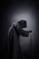 Creepy figure in hooded cloak with staff over dark misty background