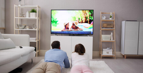 Young Happy Couple Lying On Carpet Watching Movie On Television