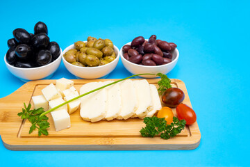 Sliced Halloumi cheese with herbs and tomato on a wooden board and pickled olives as a concept of Cypriot products