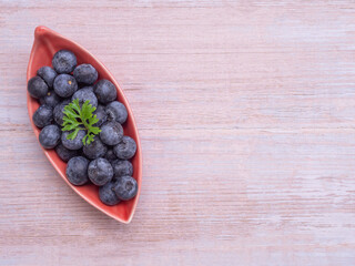Top view, fresh blueberries in leaves-shaped red plate on white wooden background. Flat lay with copy space. Concept for healthy eating and nutrition, Superfood..