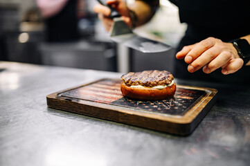 chef hand cooking cheeseburger with vegetables and meat on restaurant kitchen