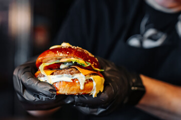 Man's hands holding burger with meat, cheese and vegetables