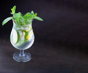 Summer mint lime refreshing cocktail mojito with ice in glass on black background copy space. Carbonated mineral water and lemon. Glass for drinks. Lemonade at the bar menu. Classic sparkle drink.
