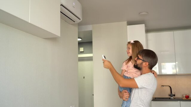 Father with little girl turn on air conditioner using remote control. Happy family adjust comfortable temperature of cooler system