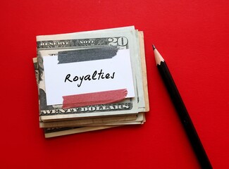 Cash money dollar and pencil on red background with note written ROYALTIES, legally payment made on using their intellectual assets, including book copyrights