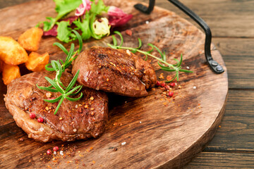 Steaks. Sliced grilled meat steak New York, Ribeye or Chuck roll with with garnished with salad and french fries on black marble board on old wooden background. Top view. Mock up.