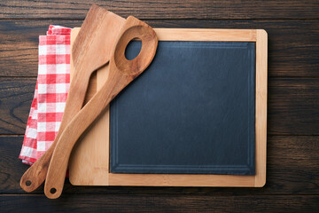 Obraz na płótnie Canvas Cutting board with kitchen spoons and red napkin and parsley, tomato for cooking on old wooden dark background. Vegetarian food, health or cooking concept. Food background with free space for text.