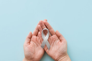 World Brain Tumor day. Person's hands are holding a gray ribbon on blue background. This is...