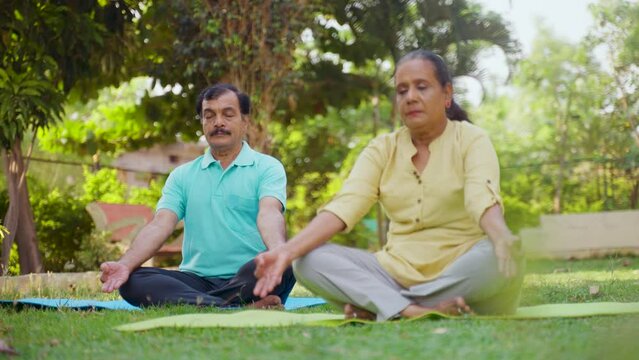 Indian senior couple doing meditation or yoga at park - concept of healthy lifestyle, mental wellness and self acre.