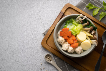 Vegetables soup with chicken ball and egg tofu in gray bowl on concrete table.