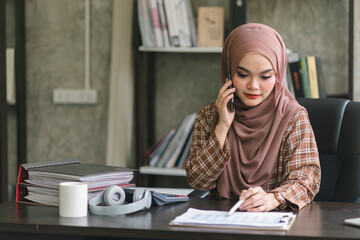 Fototapeta na wymiar A confident,beautiful, professional, millennial Muslim Asian businesswoman wearing a brown hijab is working remotely from modern office.