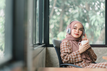 A confident,beautiful, professional, millennial Muslim Asian businesswoman wearing a brown hijab is relaxing in her office and having coffee.