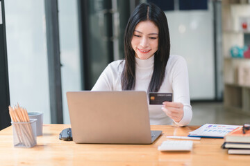 Fototapeta premium Cropped shot of female using laptop and hand holding black credit card mockup at workplace. Selective focusing