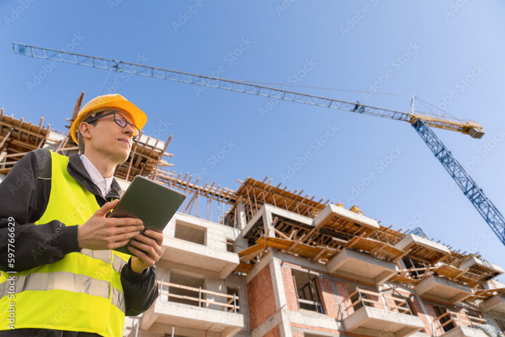 Poster Engineer with a digital tablet on the background of a building under construction	