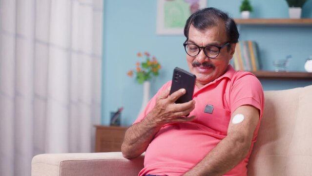 Elderly senior man checking glucose level by tapping smartphone to monitoring sensor at home - concept of health care, technology and mdicare.