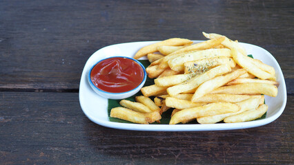 French fries with ketchup sauce in the plate on black wooden table.