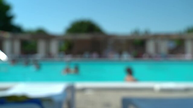 Abstract bokeh background of blurred hotel pool with blue water and swimming people. Defocused resort on hot summer day. Vacation, holiday and travel concept