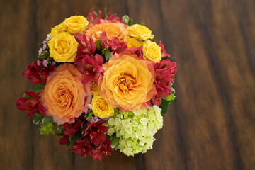 On a brown table background, a beautiful floral arrangement of orange, yellow, and red flowers with free space for text.