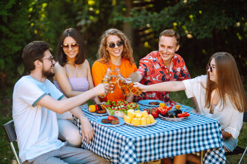 Group of young friends gathered in garden for picnic. Friends have fun, communicate in nature, drink beer. Company gathered for barbecue. Concept of vacation, lifestyle, vacation.