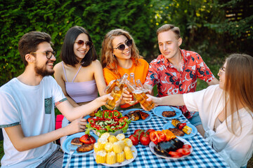 Group of young friends gathered in garden for picnic. Friends have fun, communicate in nature, drink beer. Company gathered for barbecue. Concept of vacation, lifestyle, vacation.