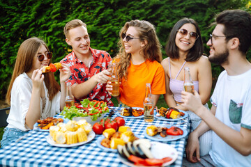 Group of young friends gathered in garden for picnic. Friends have fun, communicate in nature, drink beer. Company gathered for barbecue. Concept of vacation, lifestyle, vacation.