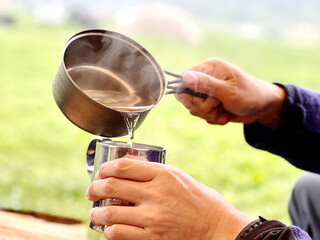 キャンプ場でコッヘルからマグカップにお湯を注ぐ手元