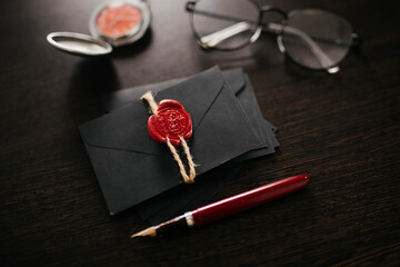 Black envelope with red wax seal and stamp on dark wooden background