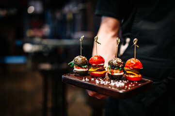 Waiter hold set mini hamburgers, mini burgers on plate in restaurant