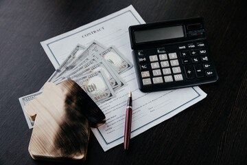 Calculator and a burn house with money on an insurance contract on a dark table. Destruction of a home and insurance services