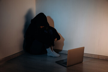 Teenager female girl sitting in a dark room in front of laptop, concept of cyber bullying