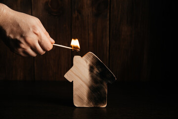Wooden house and hand with match on a dark background. Fire and real estate concept