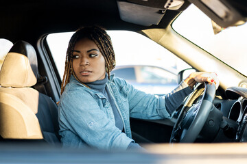 A dark-skinned young woman with braids sitting in a car looking back. Testing a new car, novice drivers. African women's travel concept. Newly taken card.
