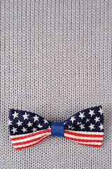 Obraz premium Bow tie with the image of the US flag on a gray knitted background.For the design of postcards, banners in clothing stores and accessories for national holidays.Independence Day.Vertical photo